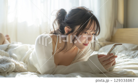 ベッドにうつ伏せに寝転がってスマホを見ている女性のイラスト素材